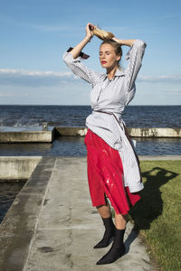 Portrait of beautiful woman standing at beach against sky