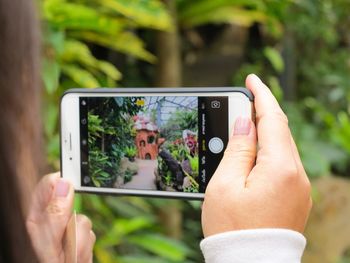 Cropped hands of woman plants with mobile phone in greenhouse