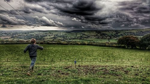 Rear view of boys on grassy field against cloudy sky