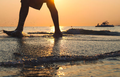 Low section of person walking at beach during sunset