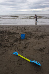 Boy with toys wading in sea against sky