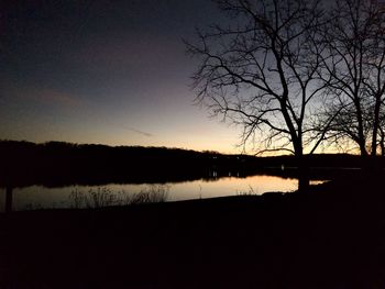 Silhouette bare trees by lake against sky during sunset
