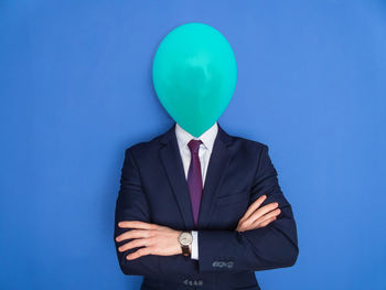 Face of businessman covered with balloon against blue background