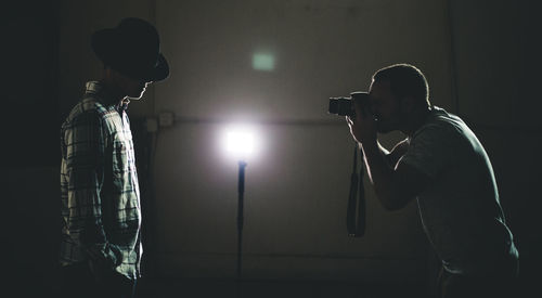 Silhouette of man photographing a male model in dark studio