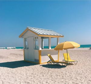 Lifeguard hut and parasol with chairs at beach against clear blue sky
