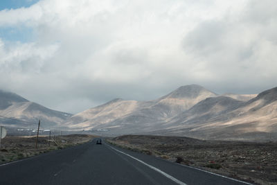 Road passing through mountains against cloudy sky