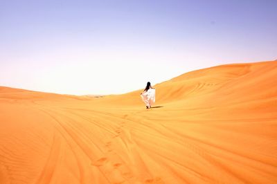 Rear view of woman walking in desert against clear sky