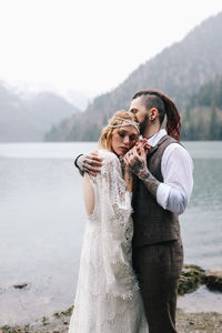 Two happy people in love the bride and groom in wedding outfits embrace by the lake and mountains