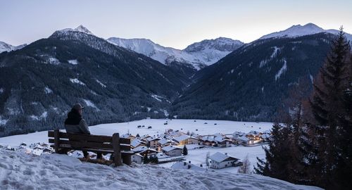 Man sitting on snow covered mountain against sky