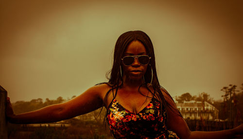 Portrait of woman wearing sunglasses standing against sky during sunset