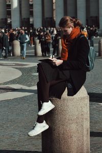 Side view of woman studying while sitting on column in city