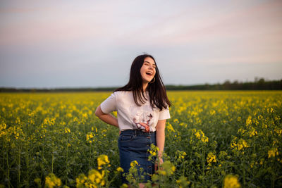 Young woman standing amidst yellow flowering plants on field against sky