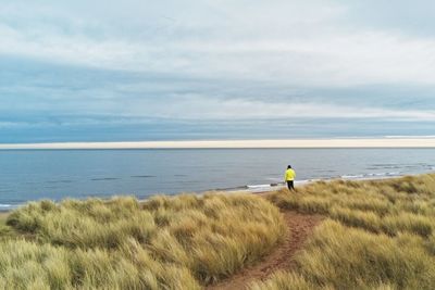 Man standing on field by sea against sky