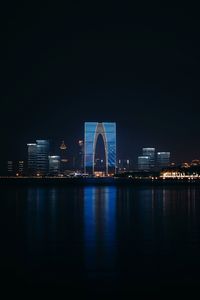 Illuminated buildings by river against sky at night