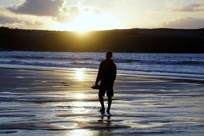 Rear view of silhouette man walking at beach during sunset