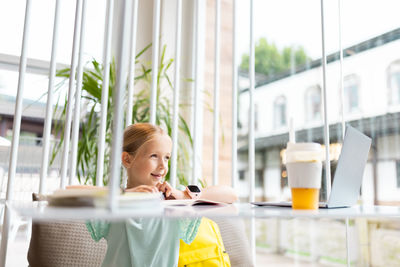 Woman looking away while sitting on table against window