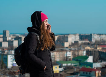 Young woman in pink hat with smartphone calling friends walking on city background millennial girl 