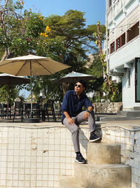 Side view of man sitting against building