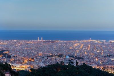 High angle view of illuminated buildings by sea against sky