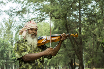 Portrait of bearded man playing violin against trees