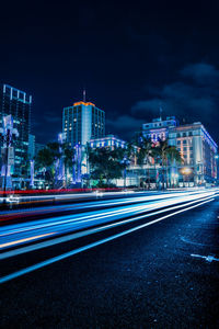 Light trails on road against illuminated buildings in city at night