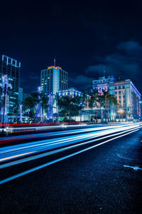 Light trails on road by illuminated buildings in city at night