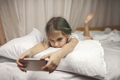 Cute girl using mobile phone while lying on bed at home