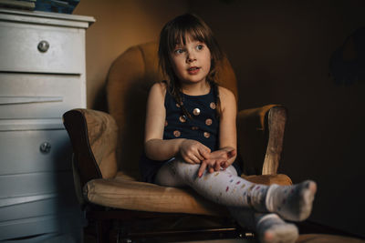 Girl looking away while sitting on armchair at home