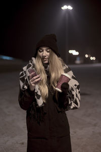 Young woman wearing warm clothing standing on road at night