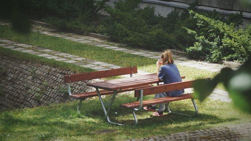 Rear view of woman sitting on bench in garden