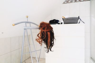 Brown wig on rack by hair dryer and bag on table in room