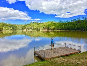 High angle view of mature man standing by lake against cloudy sky