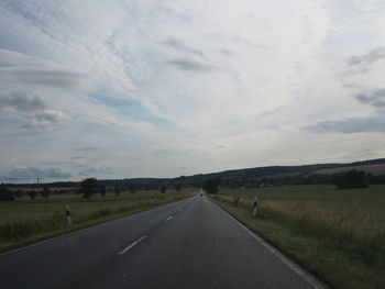 Empty road amidst field against sky