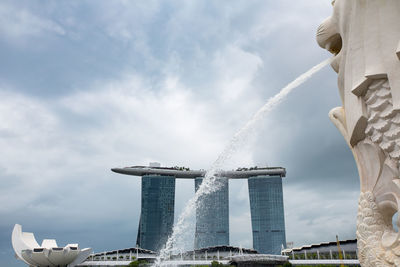 Fountain against cloudy sky in city