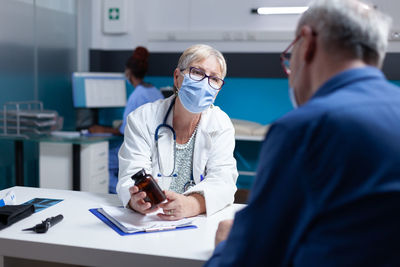 Doctor wearing mask prescribing medicine in hospital