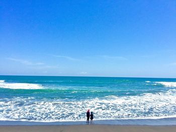 Rear view of mother and daughter standing at beach