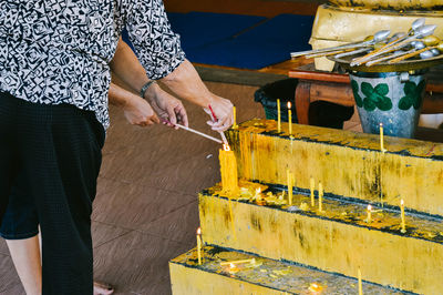 Low section of person burning candles on stone wall