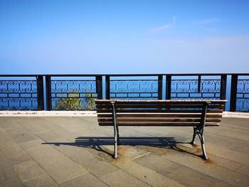 Empty bench by sea against clear blue sky