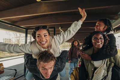 Man and woman piggybacking happy friends at railroad station platform