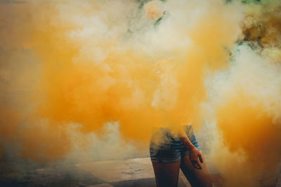 Midsection of woman standing amidst yellow smoke outdoors