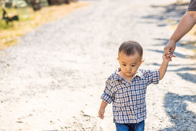 Cropped hand of man holding cute baby boy walking on dirt road