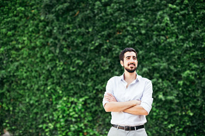 Young man with arms crossed standing against plants at park