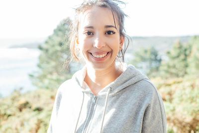 Portrait of young woman standing against trees