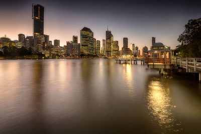 Illuminated buildings by river against sky in city