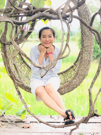 Portrait of smiling young woman sitting on tree trunk