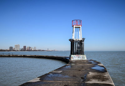 Warning light by sea against clear blue sky