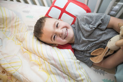 Happy toddler boy resting head on pillow in bed.