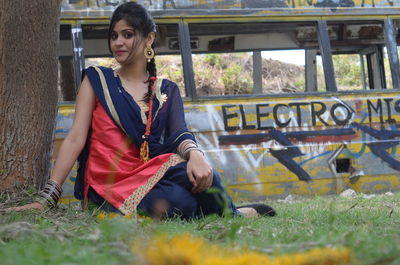 Surface level portrait of young woman in salwar kameez sitting on grassy field