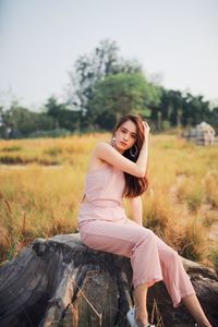 Portrait of young woman sitting on tree stump against clear sky