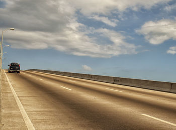 Cars on road against cloudy sky